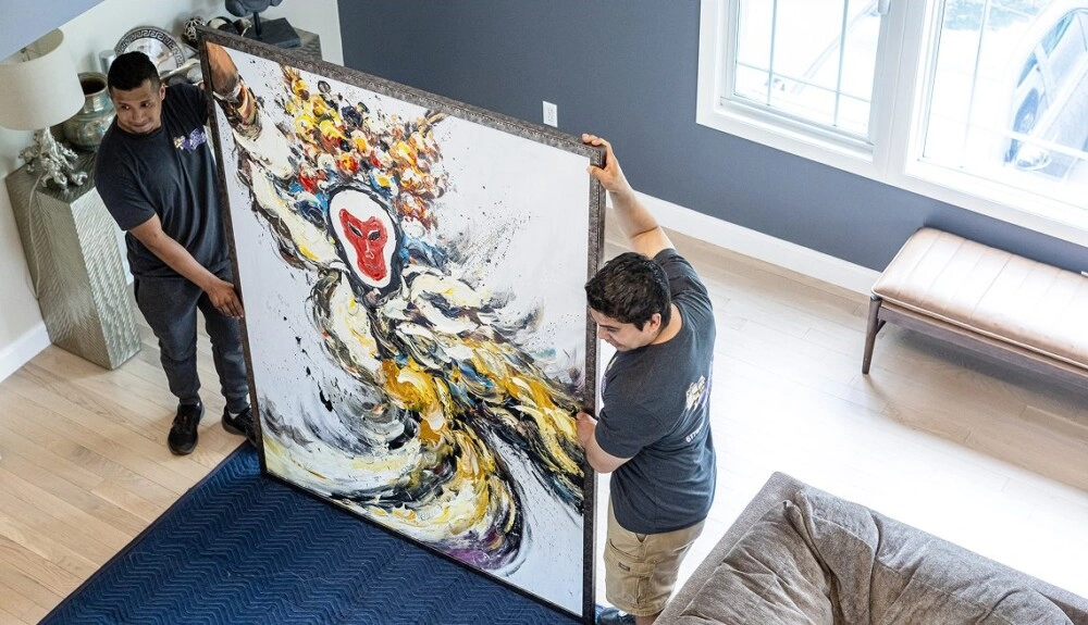 Two movers carrying a large framed painting inside a home