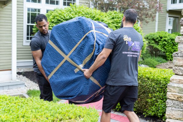 Movers carrying a heavy table in protective padded wrap